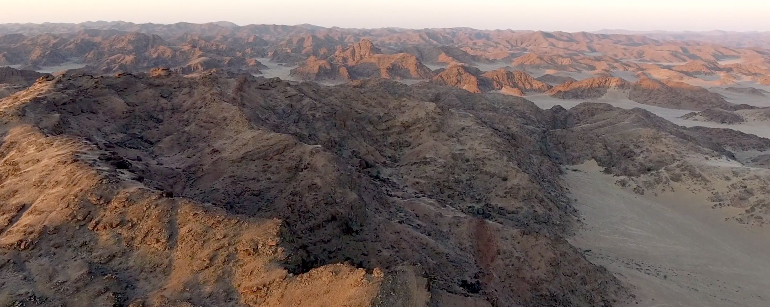 The red rocks of the desert mountains of Namibia gleam under the rising sun.