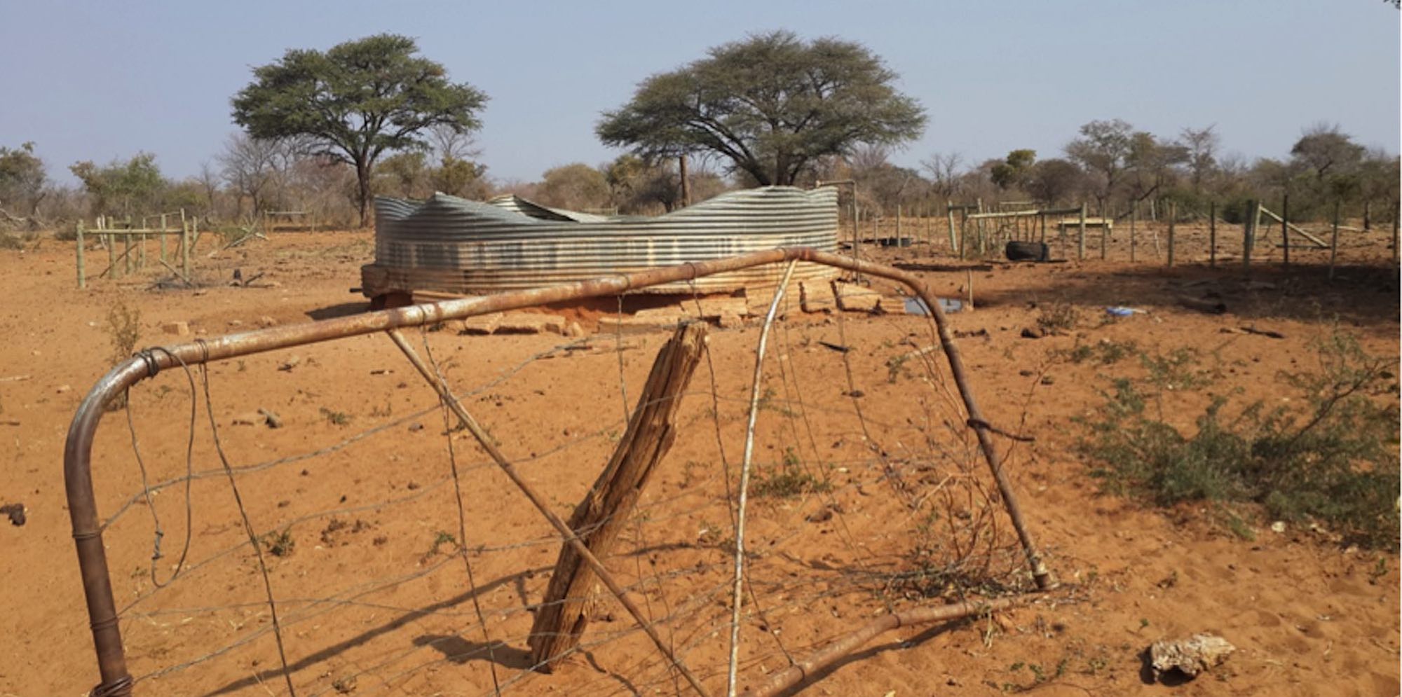 A broken down gate being held up by a piece of wood, and the shattered remains of a metal water tank.