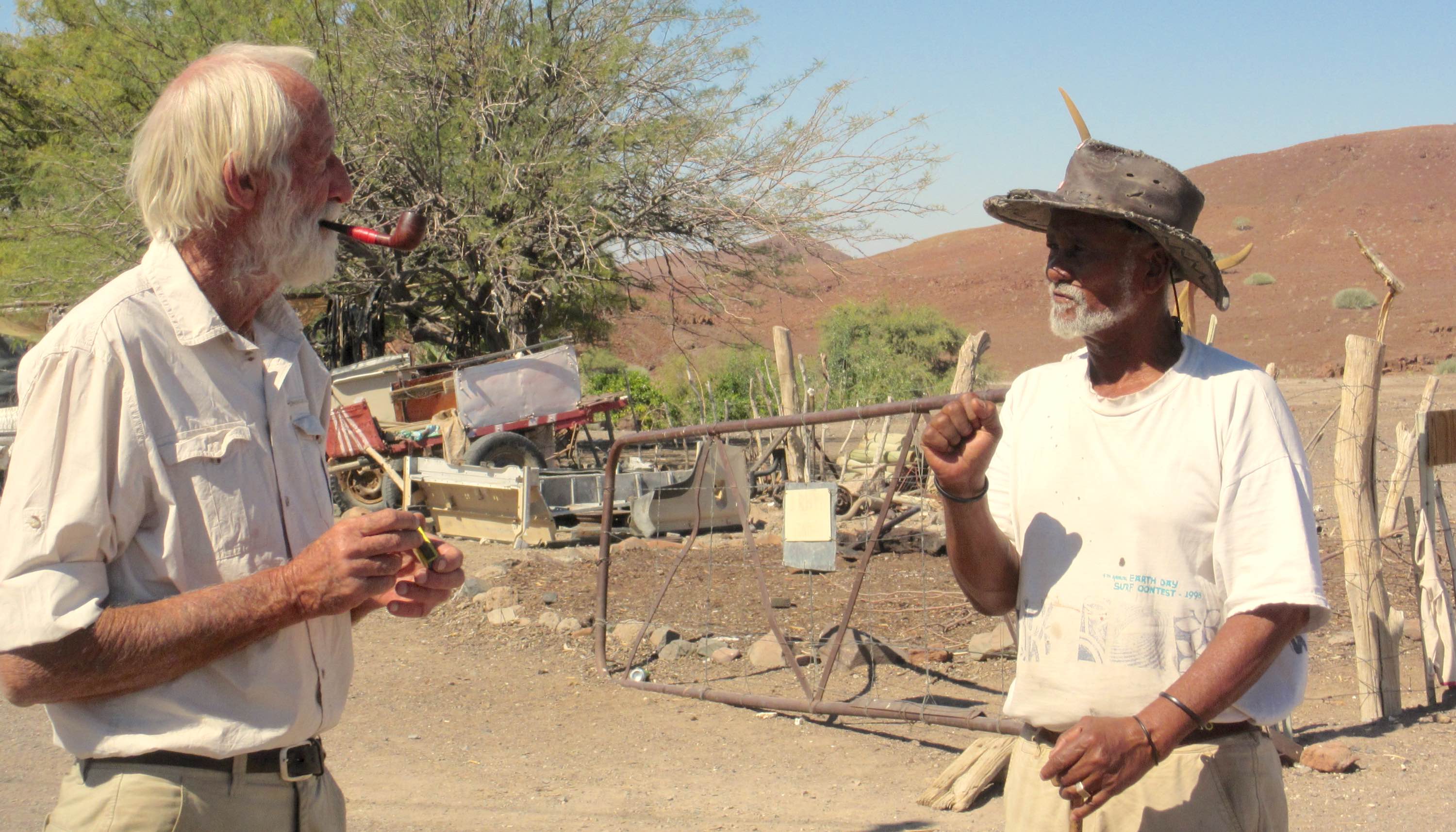 Garth strikes a match to light his pipe, while another man talks to him.
