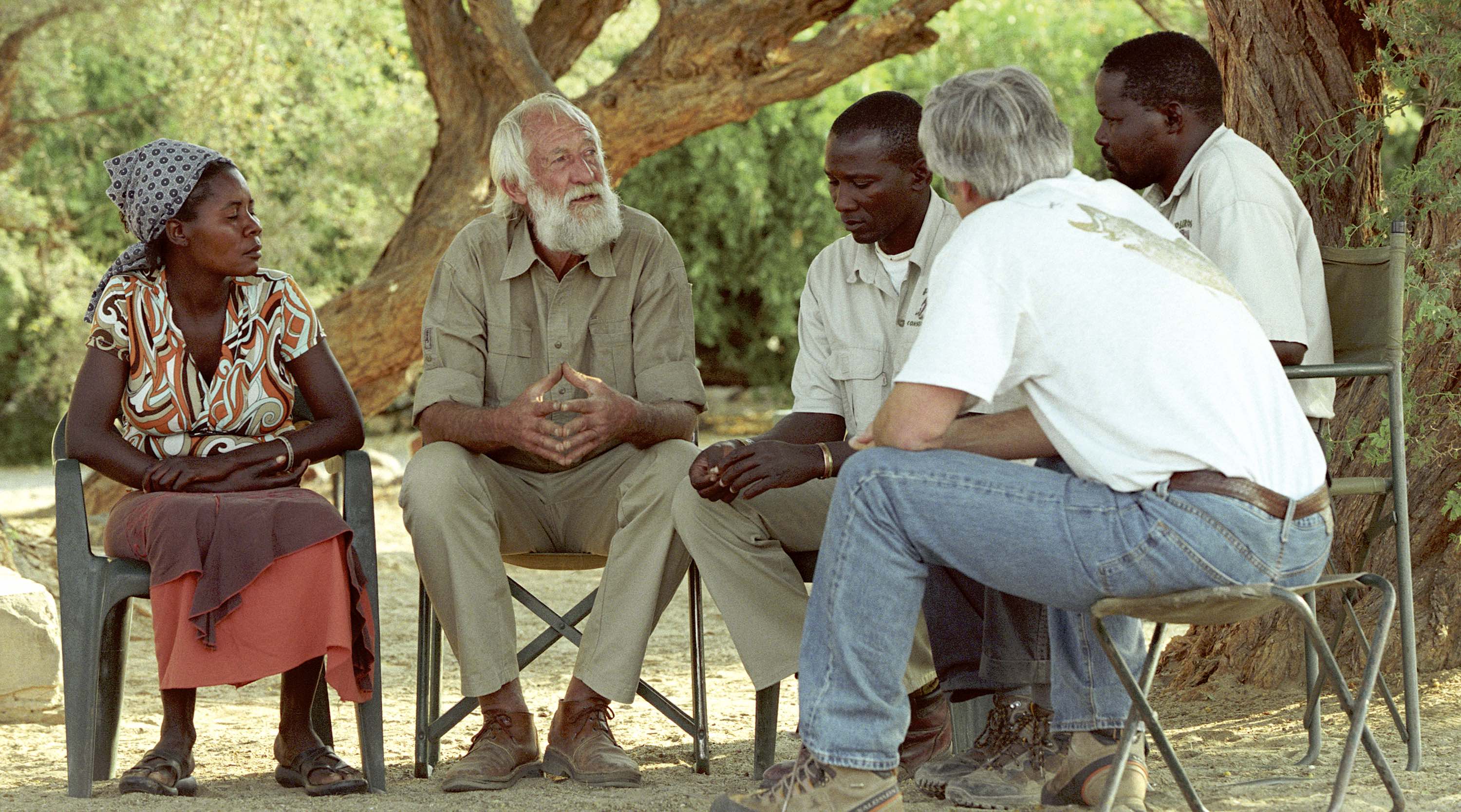 Five people sitting on camp chairs in a circle under a large tree. Garth Owen-Smith is speaking, while the others listen.