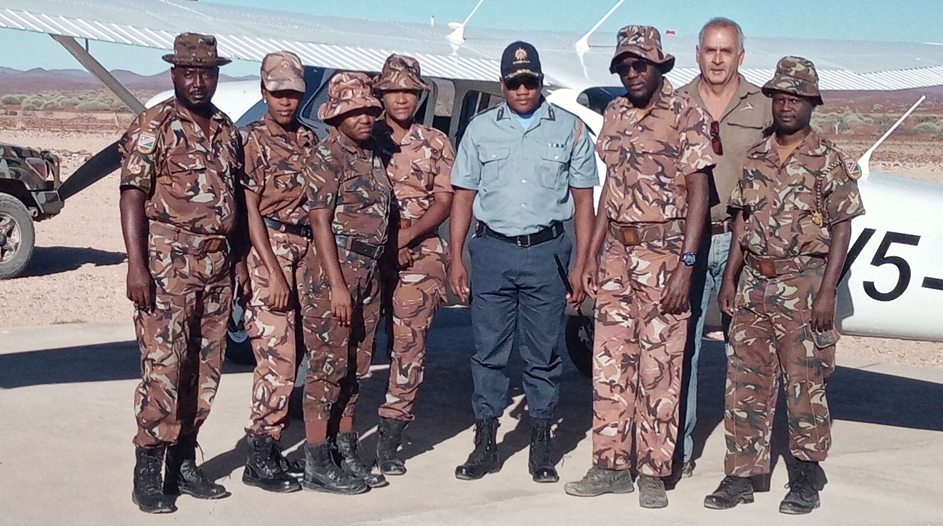 A group of eight people in uniform standing in front of a light aircraft.