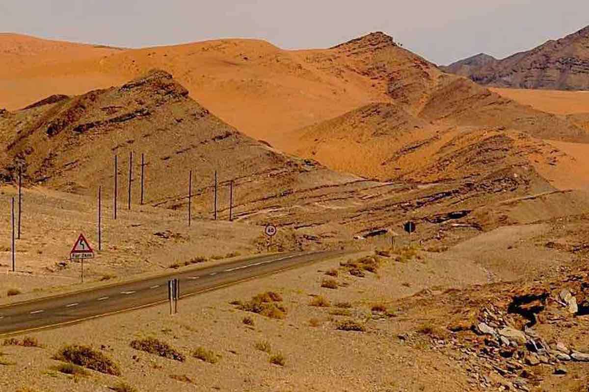 A road and pylons cut through a mountainous and desert environment.
