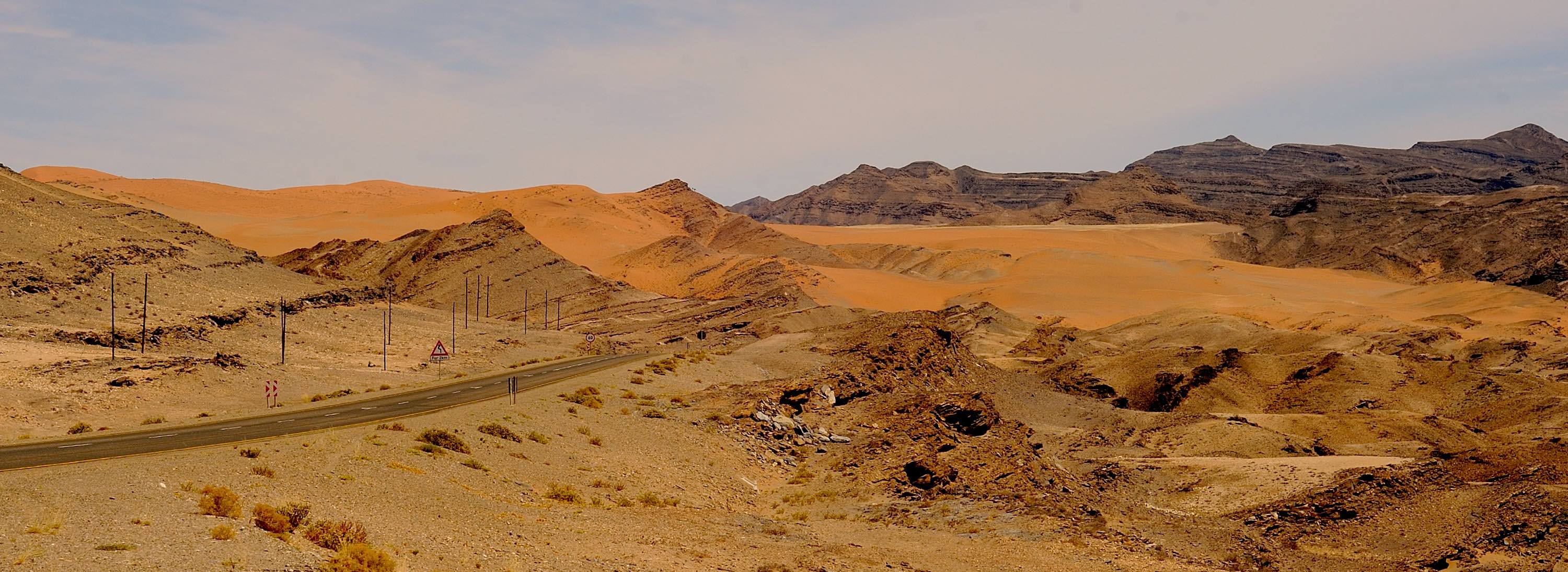 A road and pylons cut through a mountainous and desert environment.