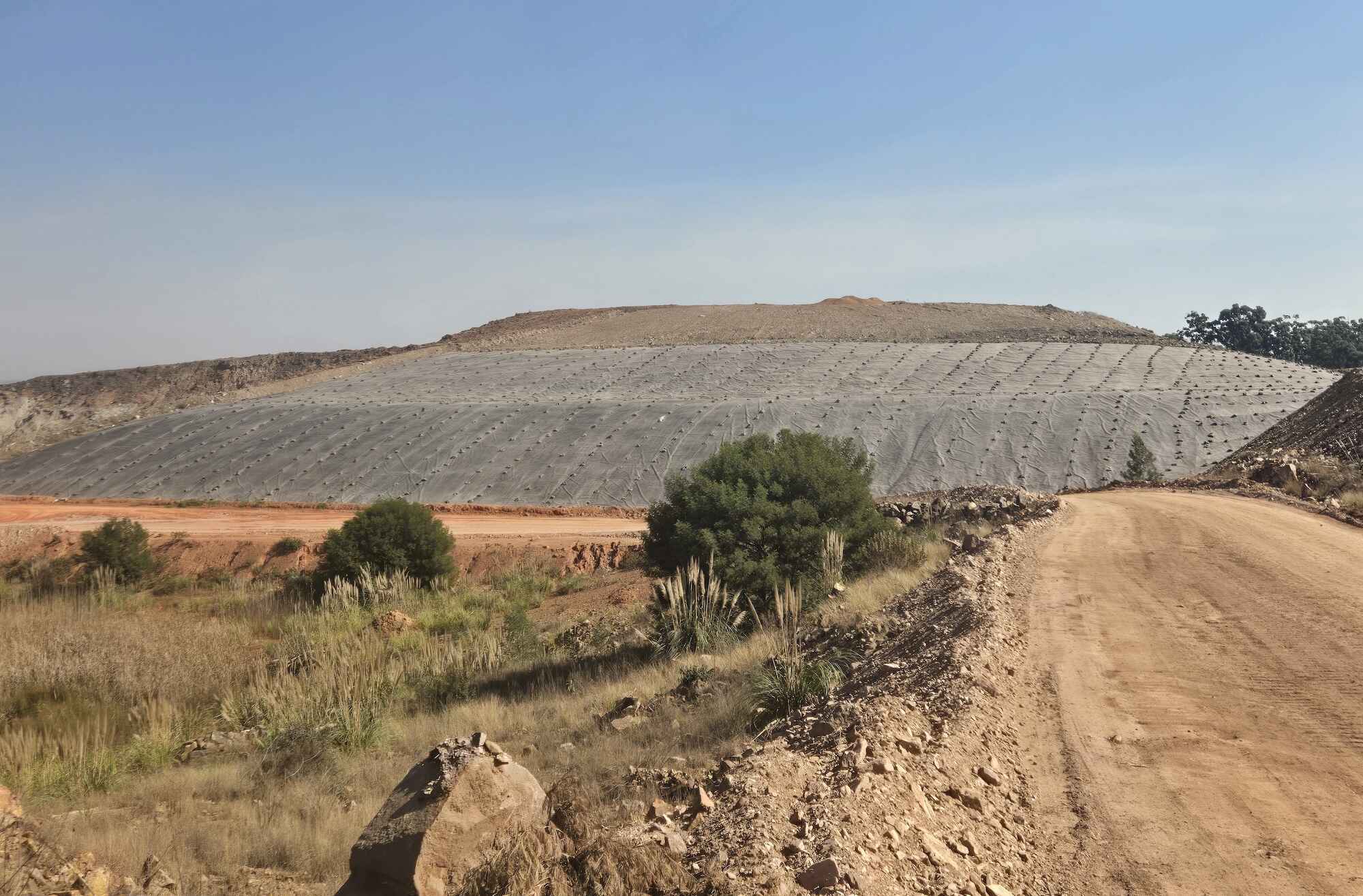 A low hill covered in impermeable sheeting and weighted down with rocks.