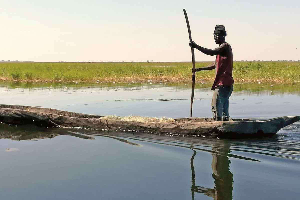 A man poles a traditional canoe through still waters.