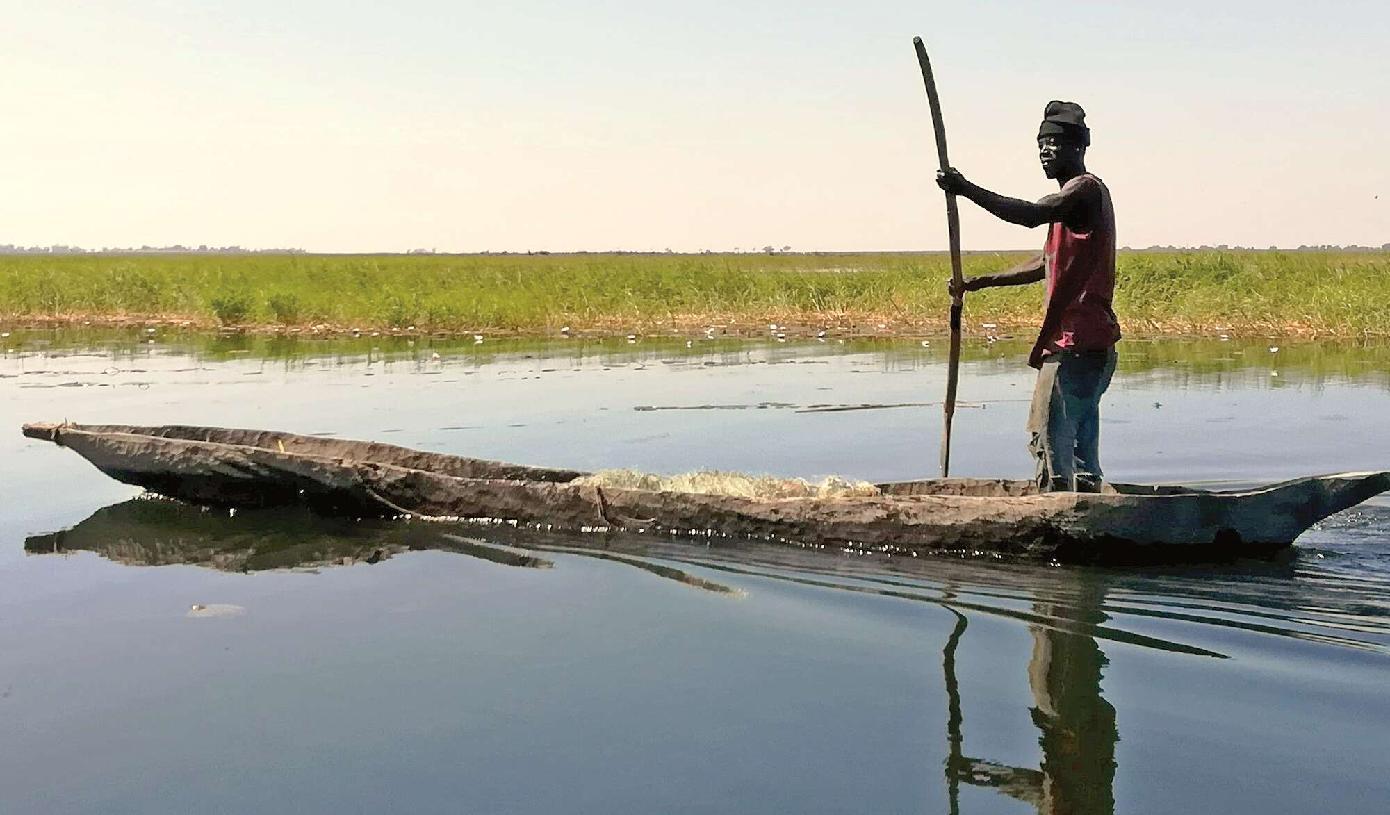 A man poles a traditional canoe through still waters.