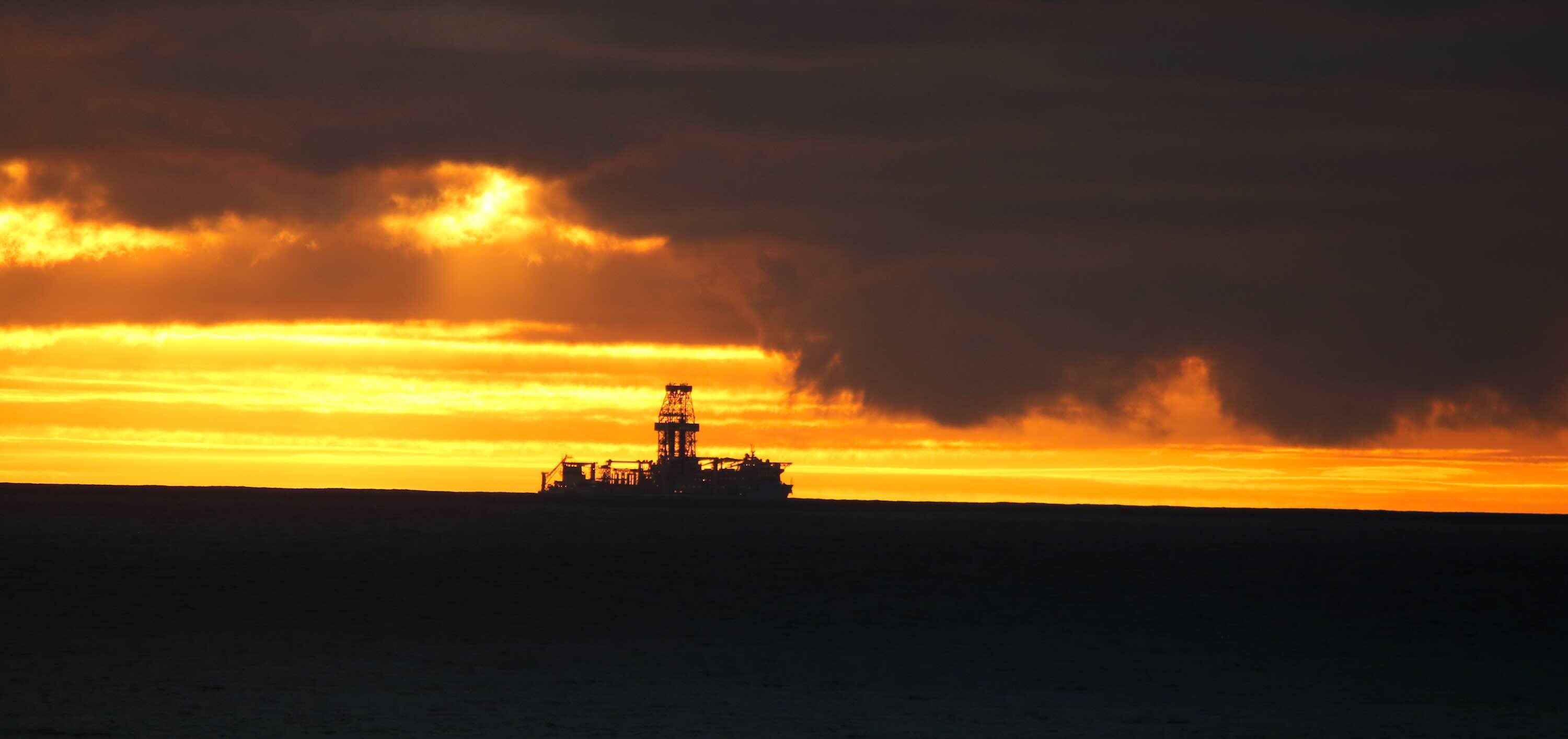 A drilling rig on the horizon at sunset.