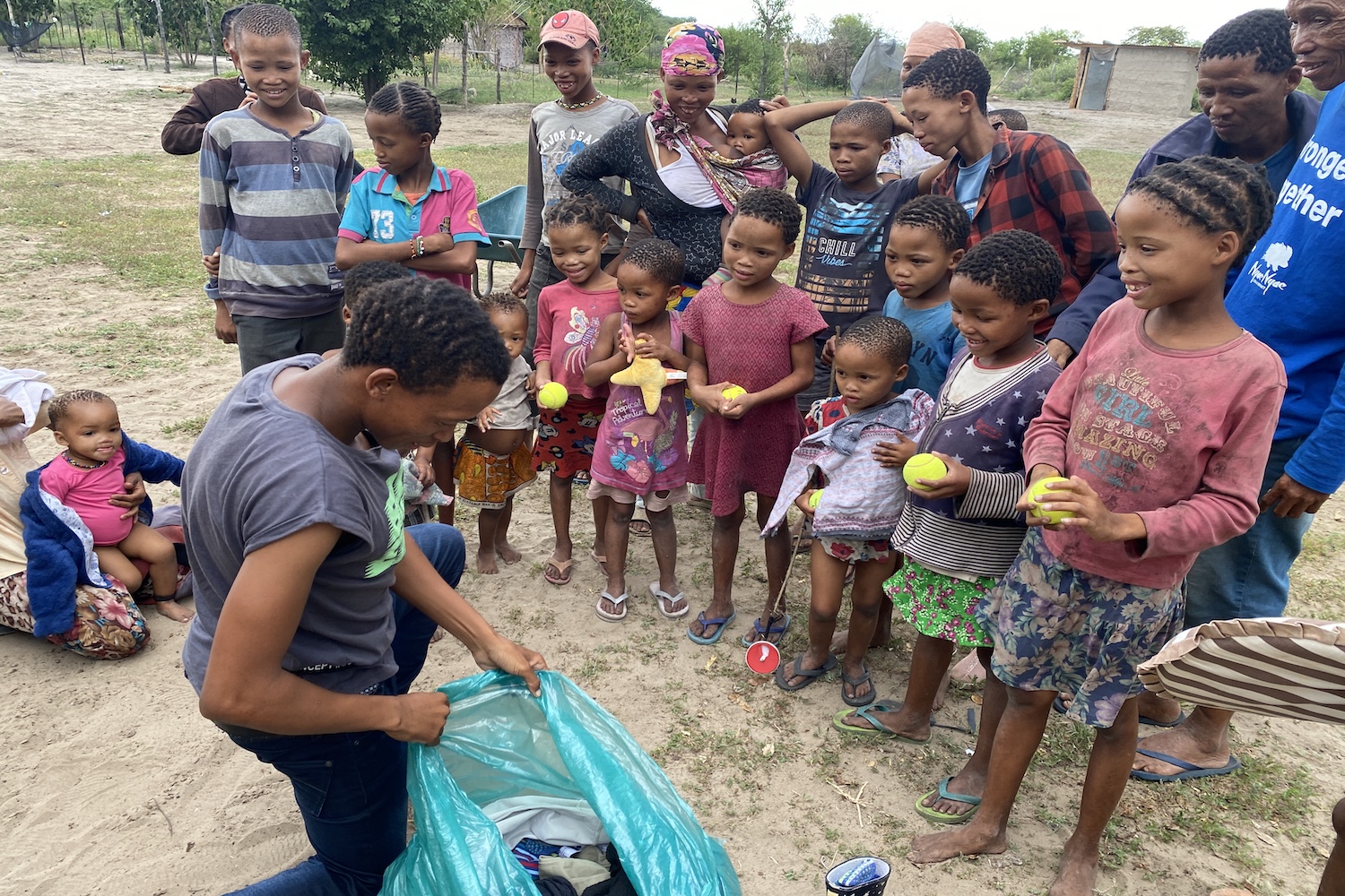 A man opens a sack in front of a group of smiling women and children.