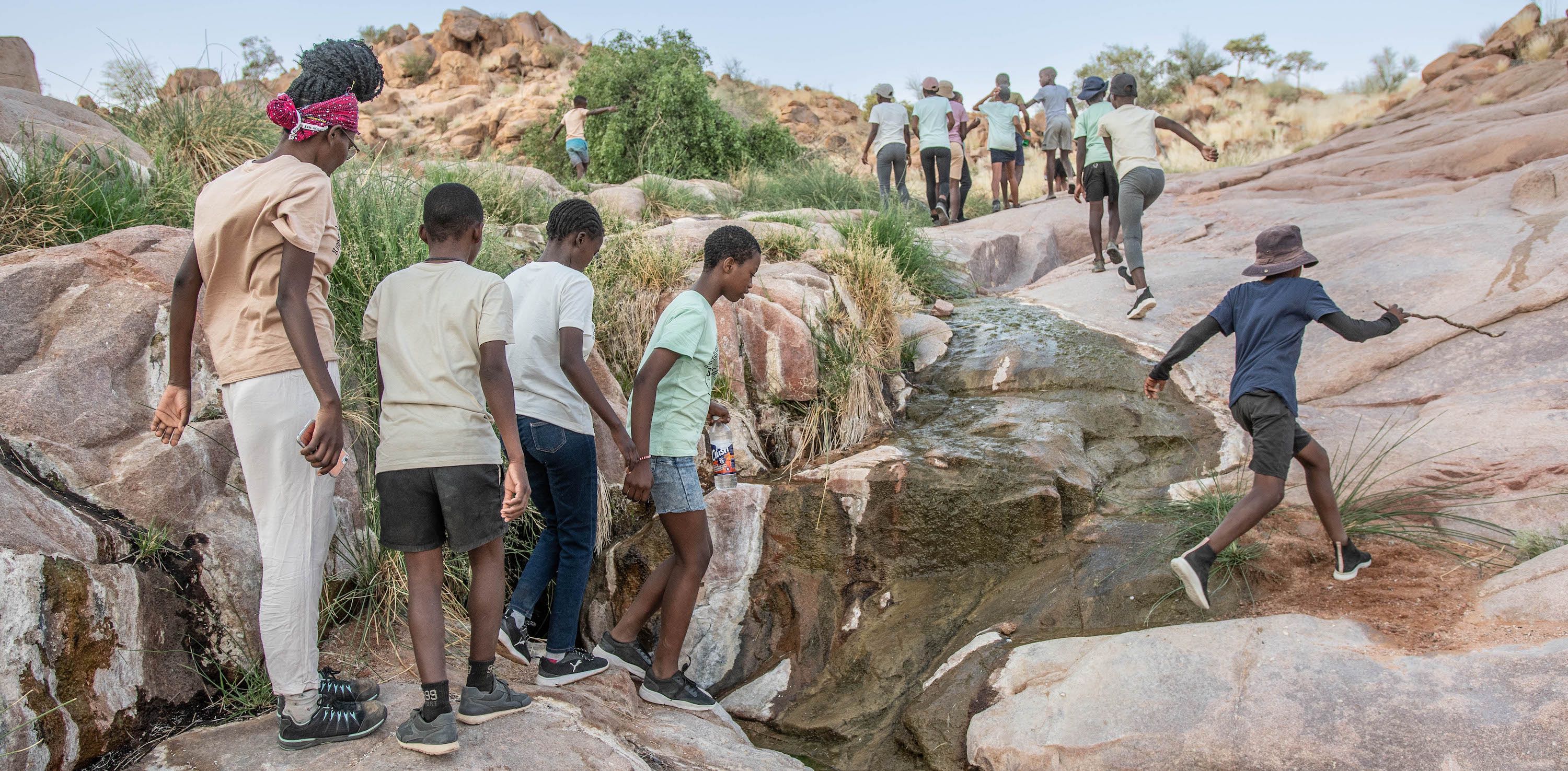 A group of children scramble up a rocky riverbed