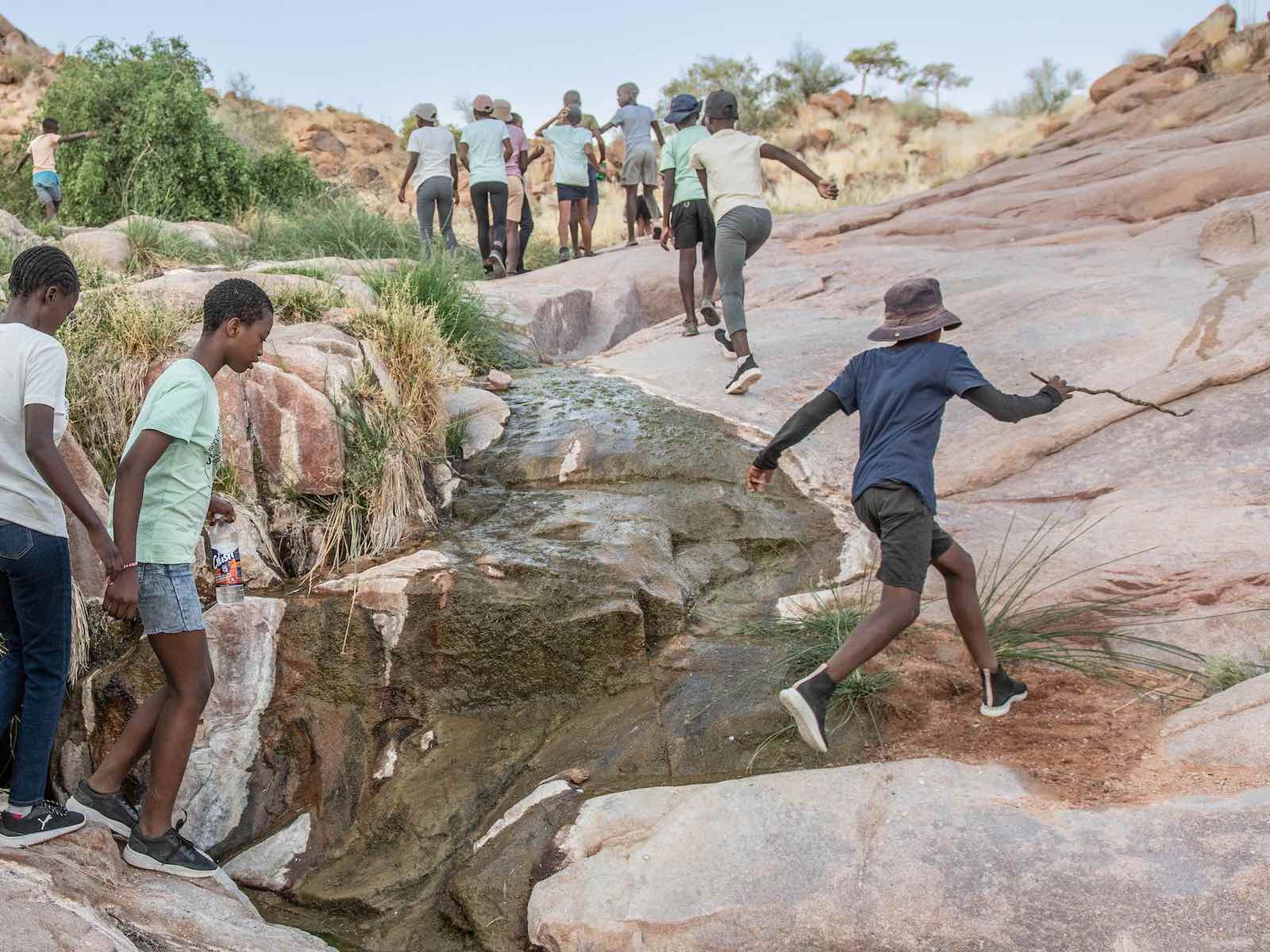 A group of children scramble up a rocky riverbed.
