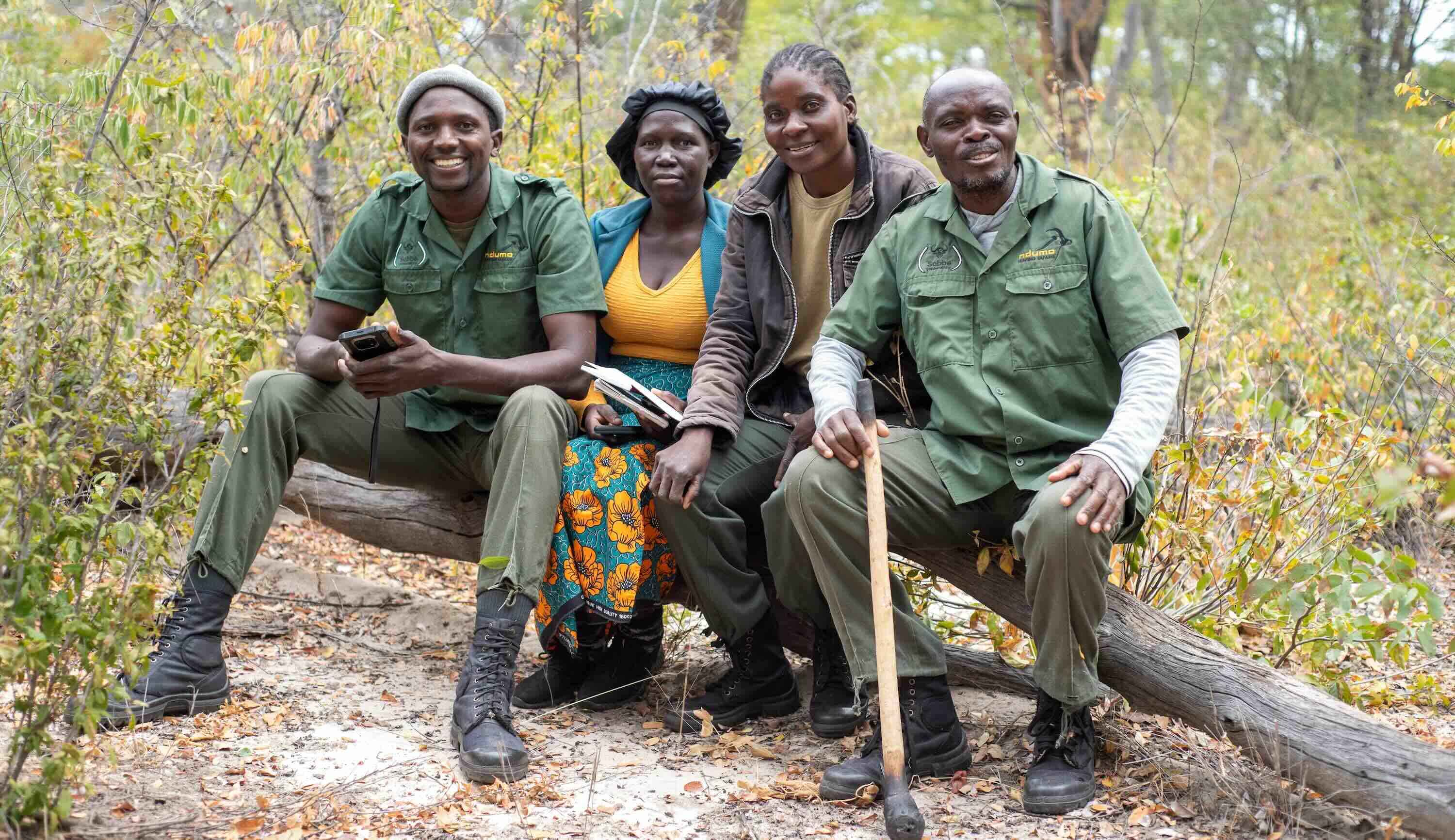 Four people sitting on a fallen tree and smiling for the camera..