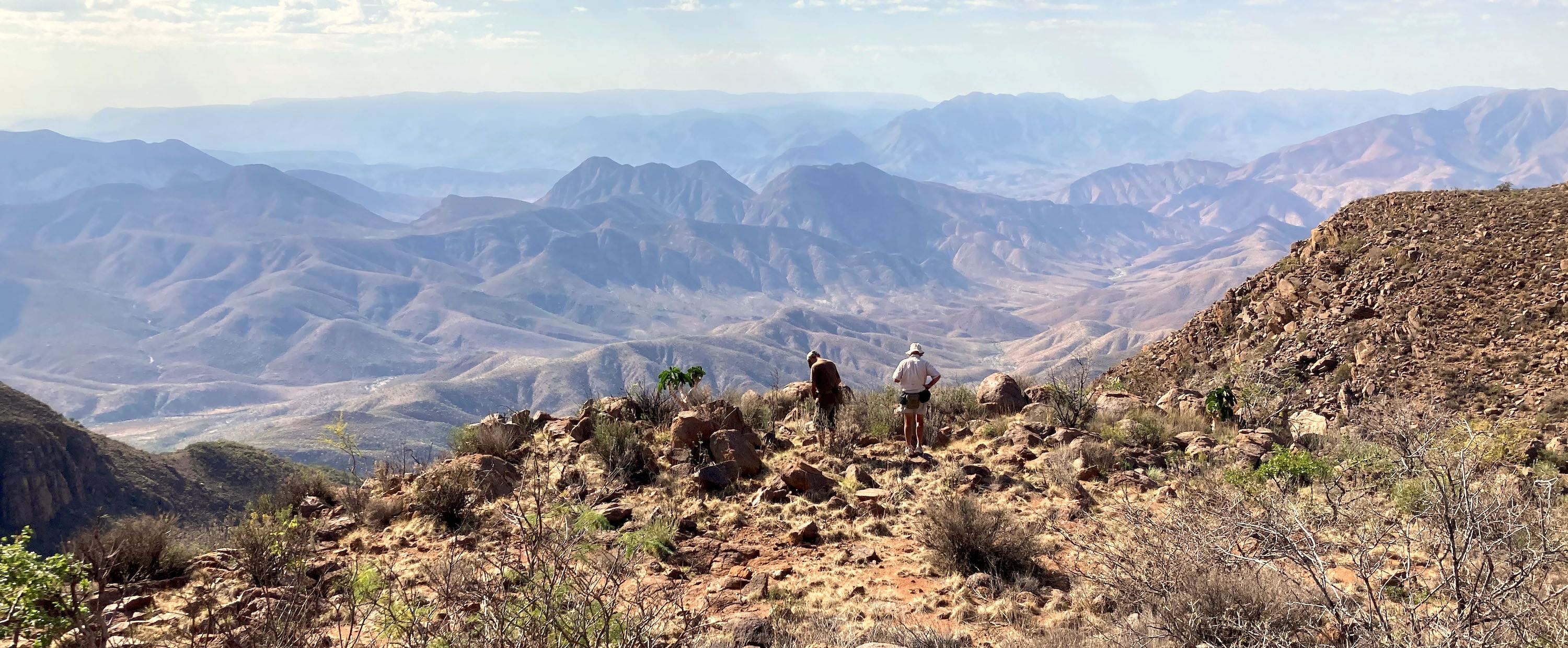 Two men gaze out across a vast mountainous landscape.